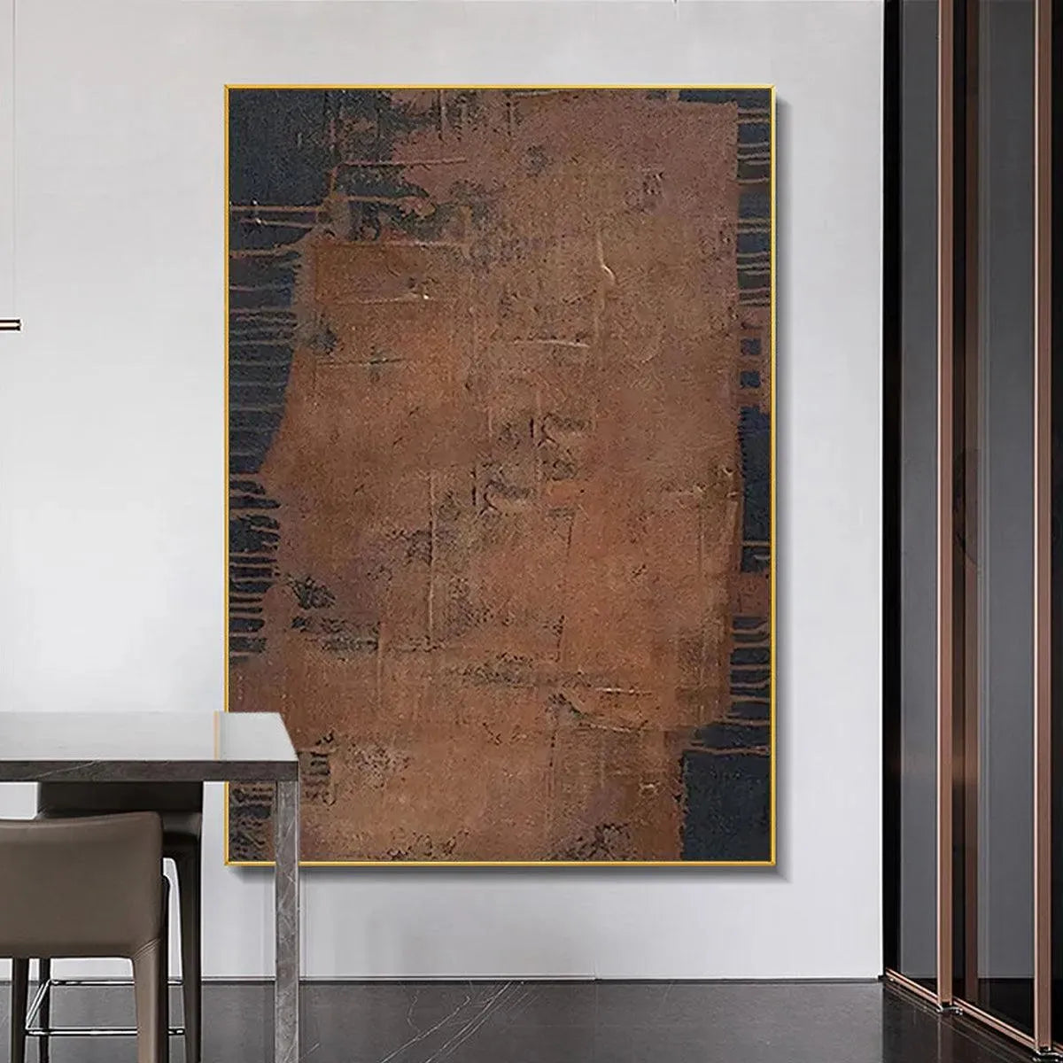 Rustic brown abstract painting with textured surface and dark accents, framed in gold, showcased in a modern room
