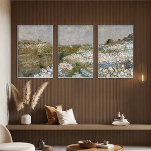 Triptych impressionist wildflower paintings above sofa, with white and blue blossoms under gray sky.