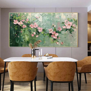 Textured impasto painting of pink cherry blossoms on a green background, framed in gold, displayed above a dining table.