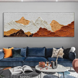 Textured impasto painting of mountain peaks in brown, white, and ochre, displayed above a blue sofa in a living room.