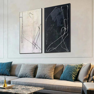 Minimalist Abstract Duo paintings: black and white line art set in black frames above sofa.