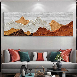 Textured impasto painting of mountain peaks in brown, white, and ochre, displayed above a grey sofa for scale and decor.