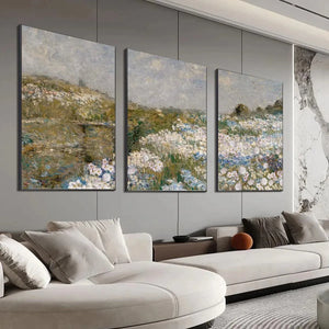 Impressionist triptych painting of a wildflower meadow with white and blue blossoms above a sectional sofa.