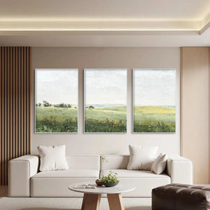 Set of 3 minimalist green field paintings, silver frames, above white sofa.