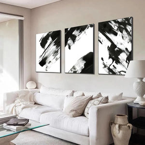 Black and white abstract triptych wall art set with bold brushstrokes above a white sofa in a modern living room.