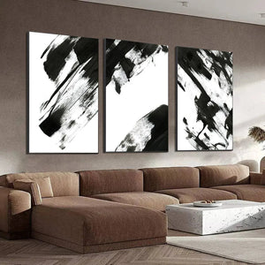 Black & white abstract triptych art with bold brushstrokes over brown sofa in living room.