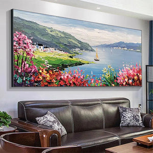Vibrant Impressionist coastal painting with flowers & sailboat, enhancing a modern living room above a dark leather sofa.