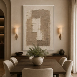Beige relief texture painting with layered abstract blocks in a white frame displayed in a refined dining room.