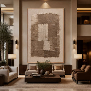 Beige relief texture painting with layered abstract blocks in gold frame displayed in a luxury hotel lobby.