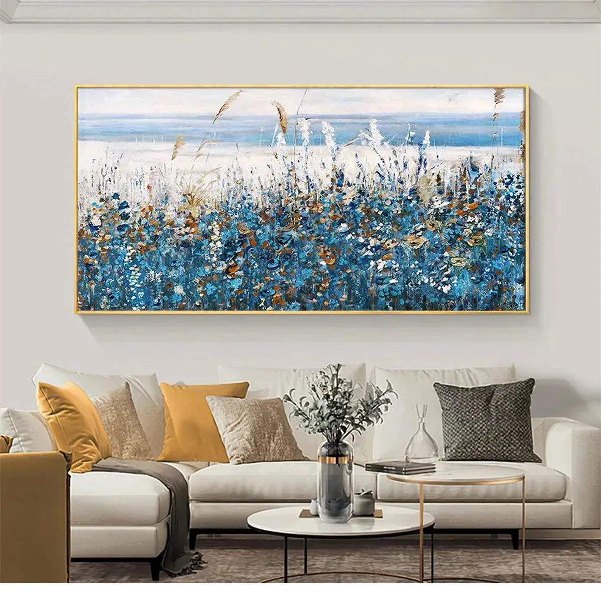 Blue Dunes coastal painting with blue wildflowers in gold frame, displayed above a gray sofa in a contemporary living room.