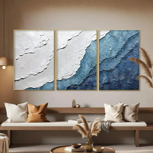 Textured abstract triptych painting set in shades of blue and white, framed in gold, evoking ocean waves.