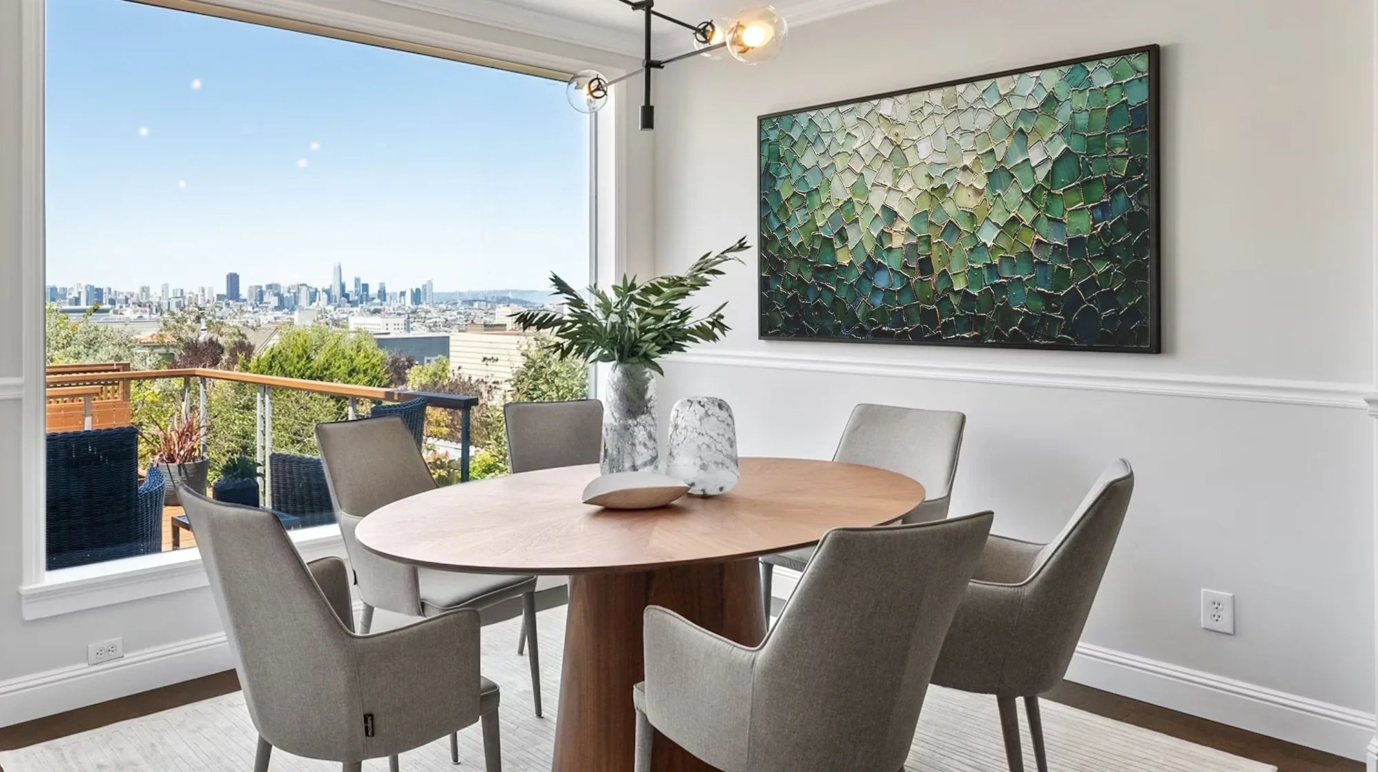 A textured abstract green and gold painting hangs on the wall of a dining room with a city view.