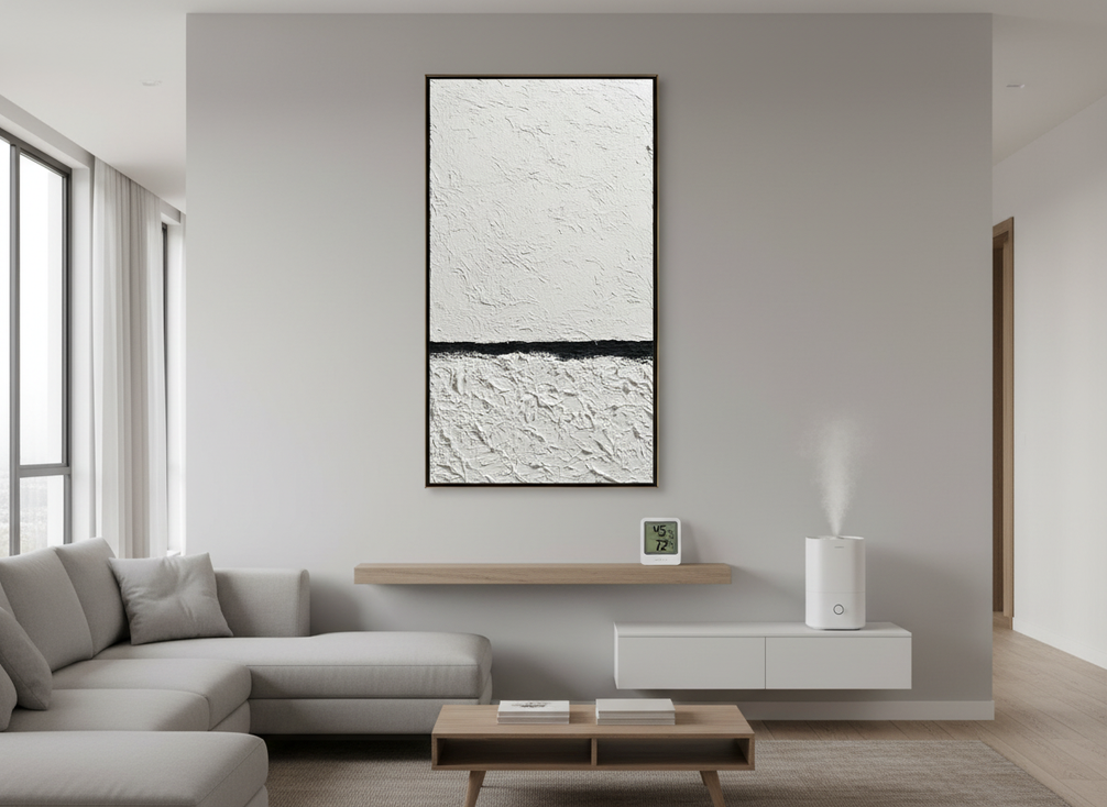 Framed textured oil painting displayed on an interior wall in a bright living room with a small humidifier and hygrometer nearby