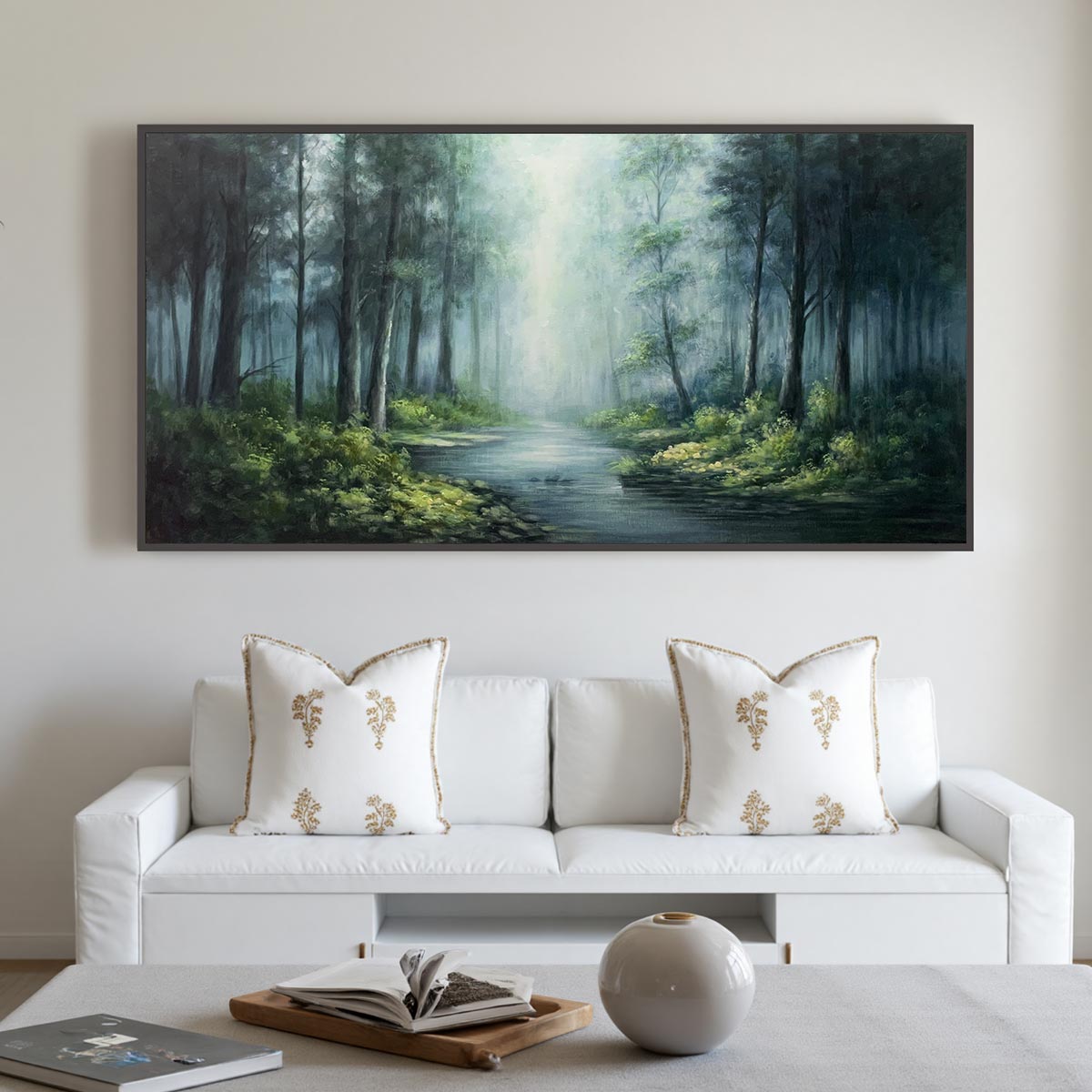 A large, atmospheric oil painting of a misty forest and stream with a central glowing light is displayed above a white sofa with embroidered pillows.