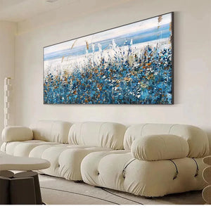 Blue Dunes coastal painting with blue flowers, dune grass, black frame, above cream sofa in modern living room.