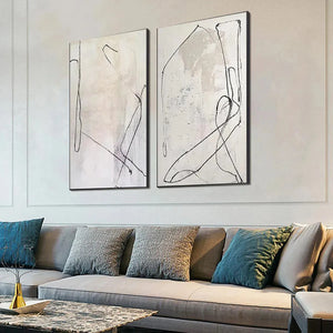 Set of 2 beige abstract paintings with black gestural lines, displayed above a sofa.