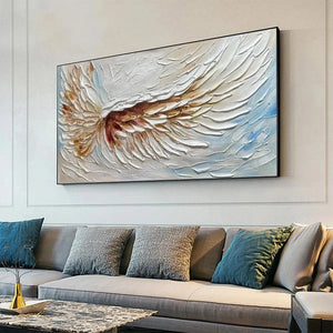 Textured white and gold impasto angel wings painting by Liam O'Connell, displayed above a grey sofa in a living room.