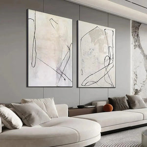 Two beige abstract paintings with black organic lines above a modern sofa in a living room.