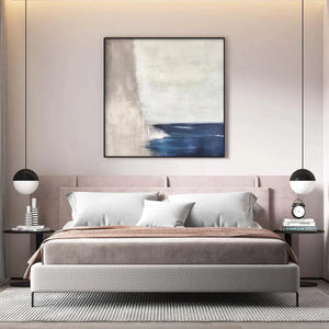 Javier Ramirez 'Serene Shore' minimalist coastal painting above a bed, blue and beige tones, modern bedroom decor.