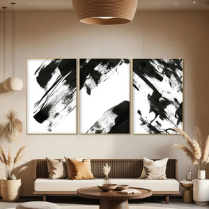 Black and white abstract triptych wall art set, vertical brushstrokes above a neutral sofa in living room.