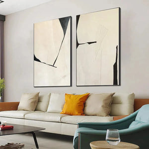 Minimalist abstract diptych, black lines on beige canvases, displayed above a cream sofa in a living room.