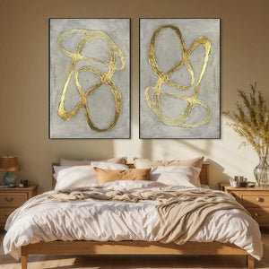 Two vertical abstract paintings with textured gray backgrounds and bold raised gold lines, displayed above a wooden bed.
