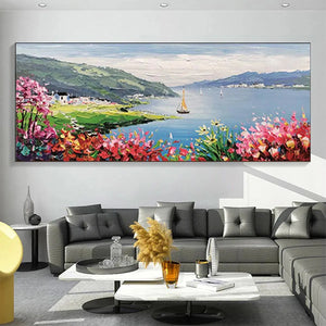 Seaside Charm impressionist coastal painting with vibrant flowers, sailboat & village, displayed above modern gray sofa.
