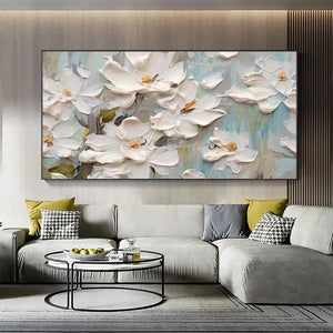 Panoramic textured painting of white magnolia blossoms with impasto strokes and golden centers, displayed above a gray sofa.