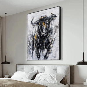 Textured black, white, and gold impasto painting of a charging bull. Vertical wall art above a bed.