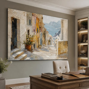 Hand-painted Mediterranean coastal village oil painting with thick palette knife texture, framed in black, displayed above a wooden desk in a modern home office.