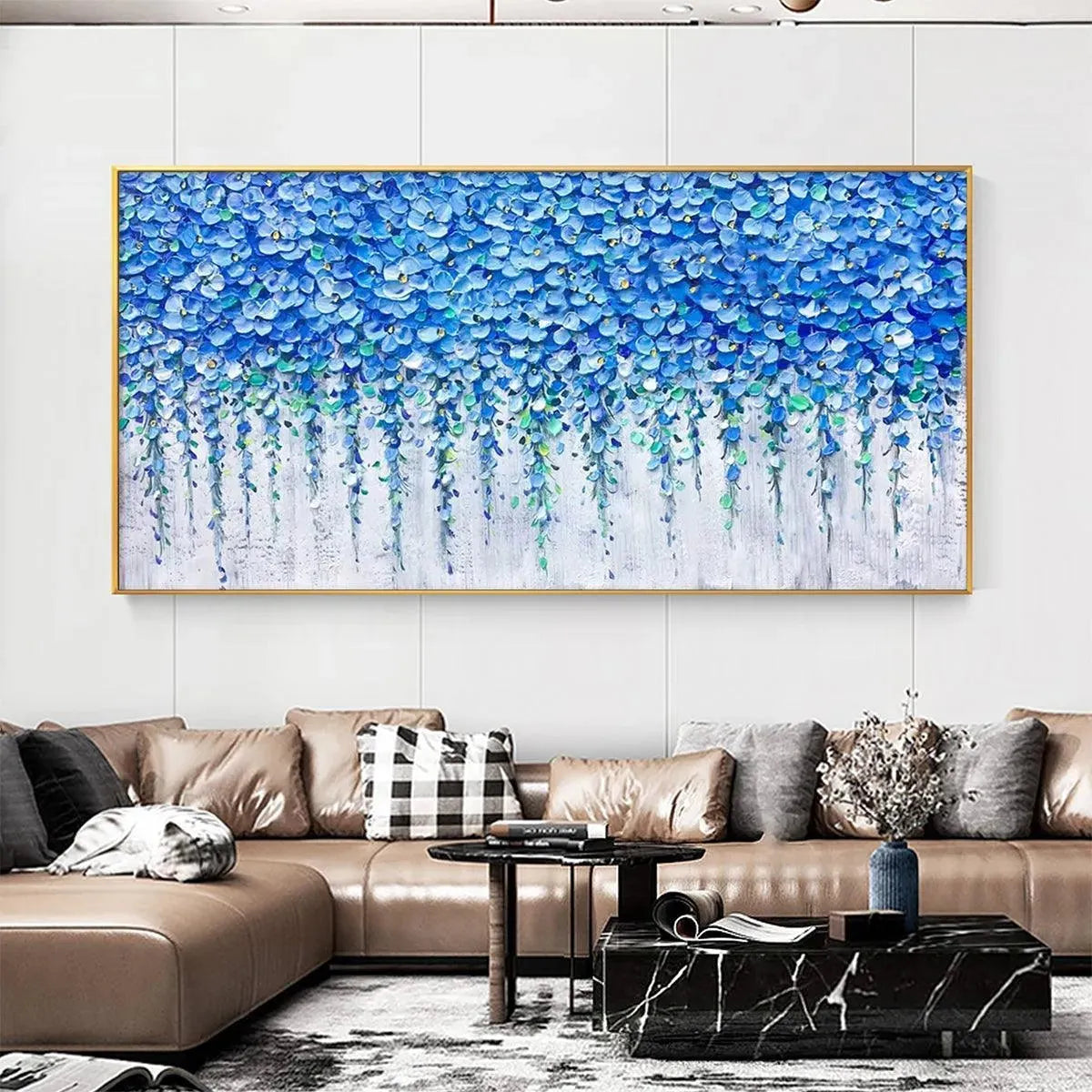 Blue Wisteria painting by Elodie Dubois, featuring cascading blue floral blossoms in a gold frame over a brown leather sofa.