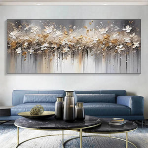 Panoramic abstract floral painting, white and gold blossoms, dripping paint, displayed above blue sofa in modern living room.