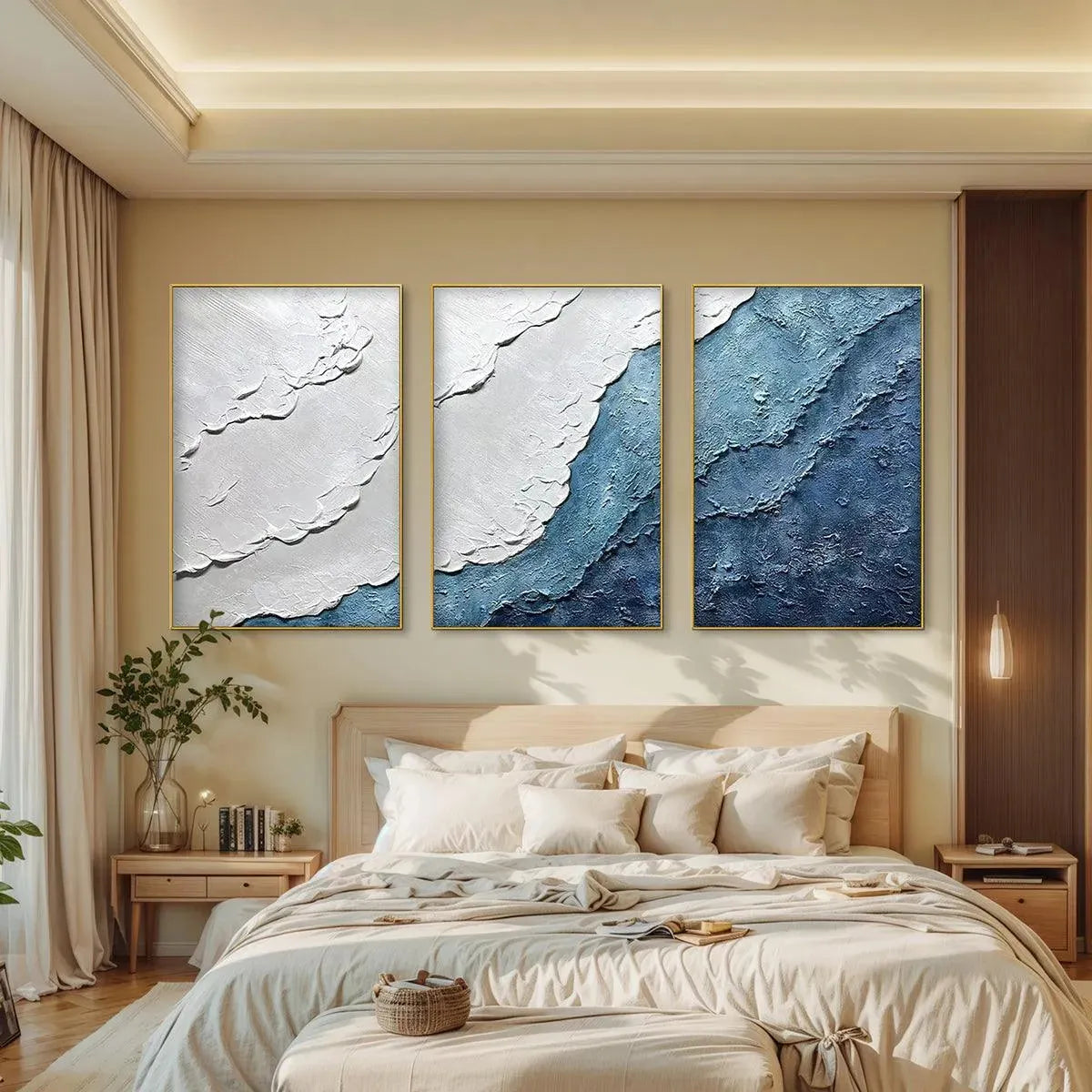 Textured seascape triptych abstract paintings in blue and white, framed in gold, above a bed in a bedroom.