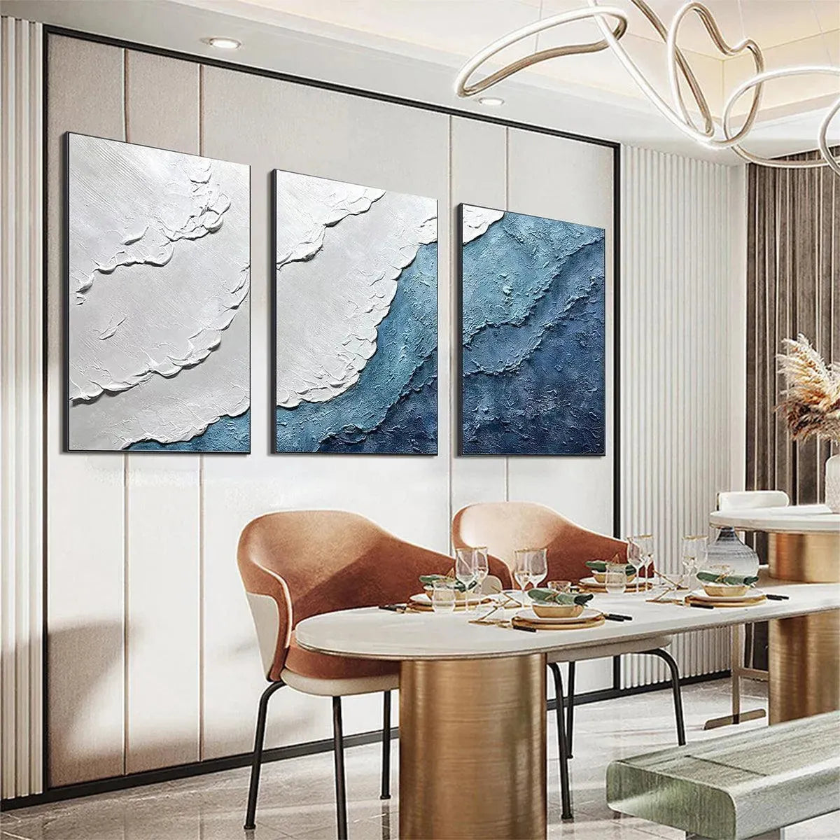 Textured abstract triptych painting in blue and white, evoking ocean waves, displayed in a dining room lifestyle setting.