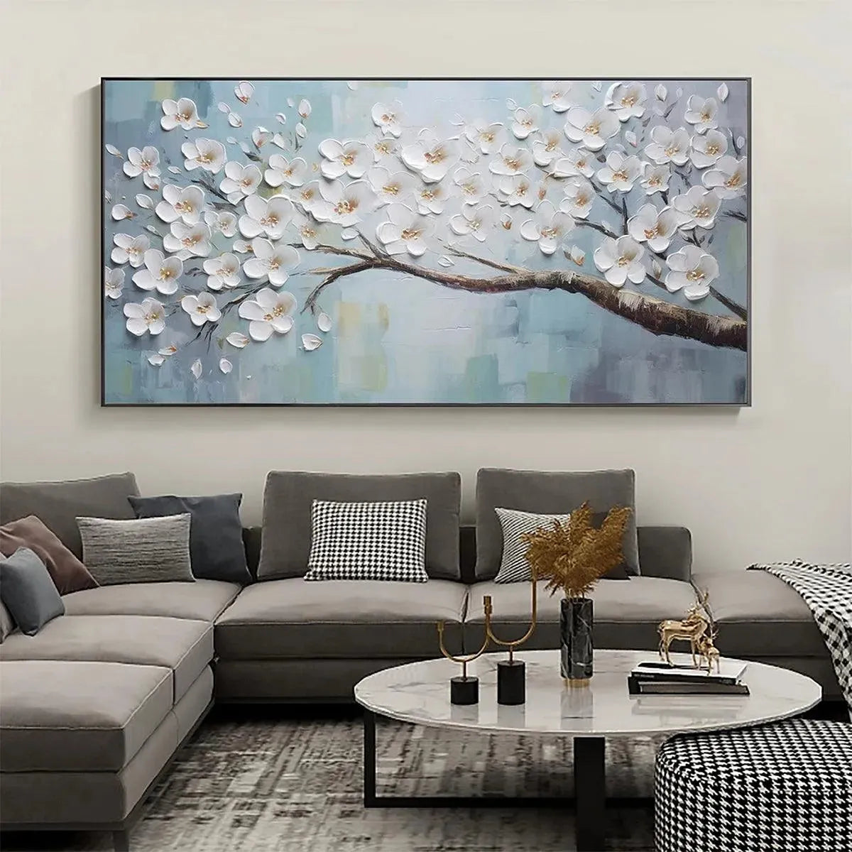 Large textured White Blossoms floral painting with blue background, styled above a sofa in a modern living room.